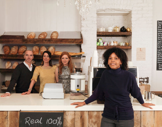 Business owner standing confidently with smiling employees inside their store, representing small businesses for sale worldwide.