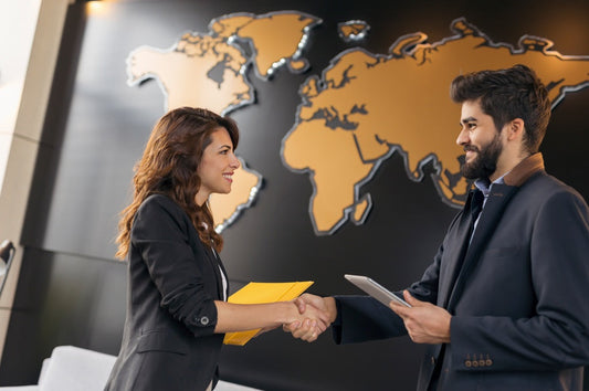 Businessman and businesswoman shaking hands in front of a world map, symbolizing global business partnerships and international deals.