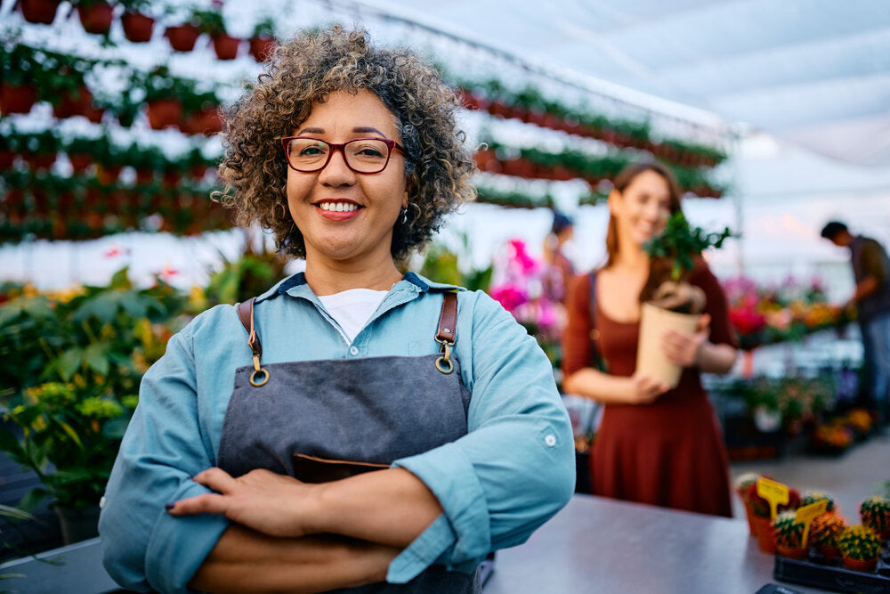 Confident plant nursery owner smiling and talking with a customer, representing small businesses for sale by owner without a broker.