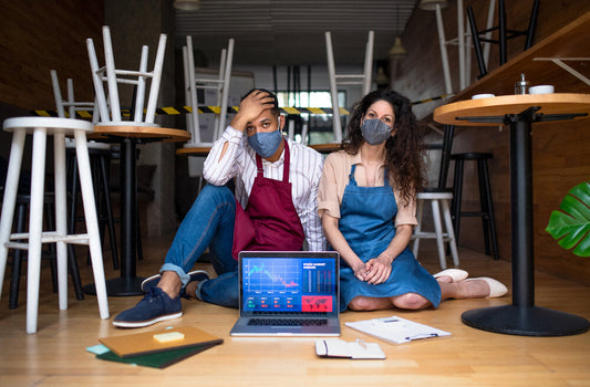 Frustrated coffee shop owners sitting in a closed café, representing distressed small businesses facing financial difficulties.