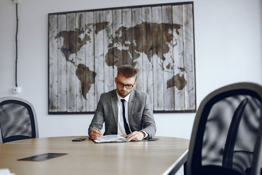 Man with glasses working at a desk in a modern office, representing global businesses for sale.