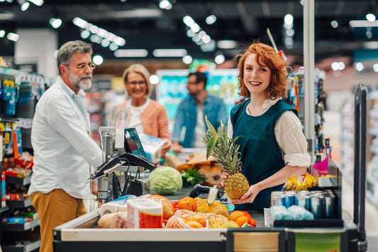 Smiling cashier holding a pineapple at checkout counter, representing retail business opportunities on a global buy and sell marketplace.